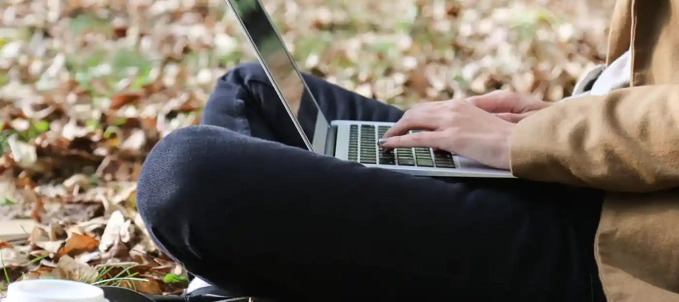A man sitting in October leaves with a laptop